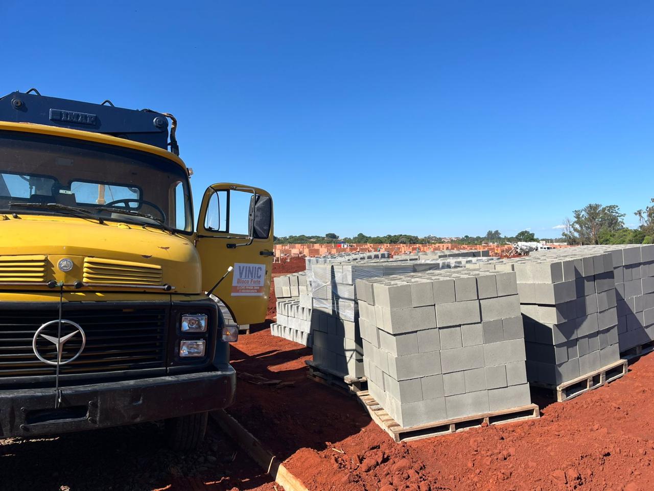 Caminhão Vinic Bloco Forte com guindaste articulado descarregando blocos em obra de loteamento na região de Santa Bárbara